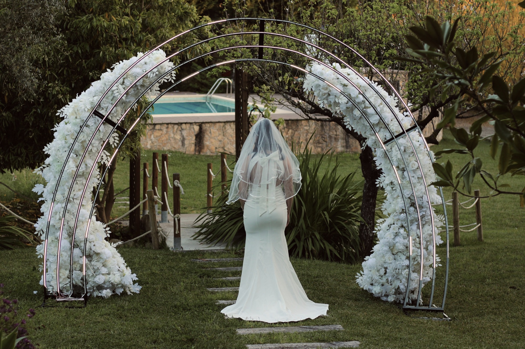 Noiva vista de costas sob um arco floral no jardim da Quinta O Refúgio